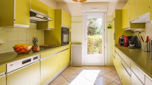 A kitchen with yellow cabinets, a built-in oven, a microwave, and a fruit bowl on the counter. - Villa Repose by Villa Plus (Argeliers)