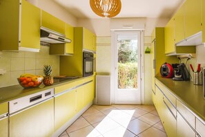 A kitchen with yellow cabinets, a built-in oven, a microwave, and a fruit bowl on the counter. - Villa Repose by Villa Plus (Argeliers)