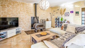A living room with a stone wall, a fireplace, a TV, a sofa, and a bookshelf. - Villa Repose by Villa Plus (Argeliers)