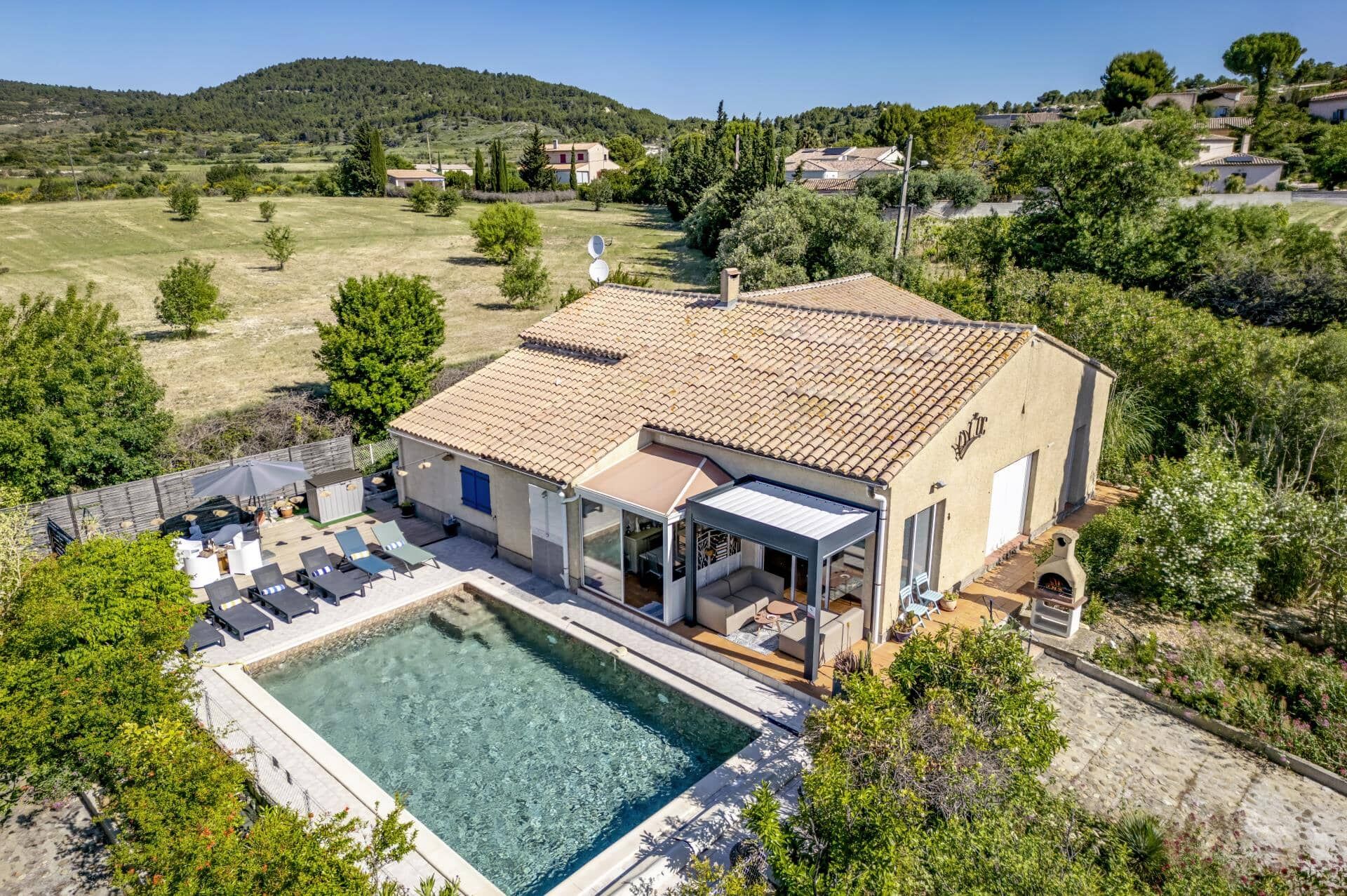 A villa with a swimming pool, outdoor seating, and a view of the surrounding countryside.