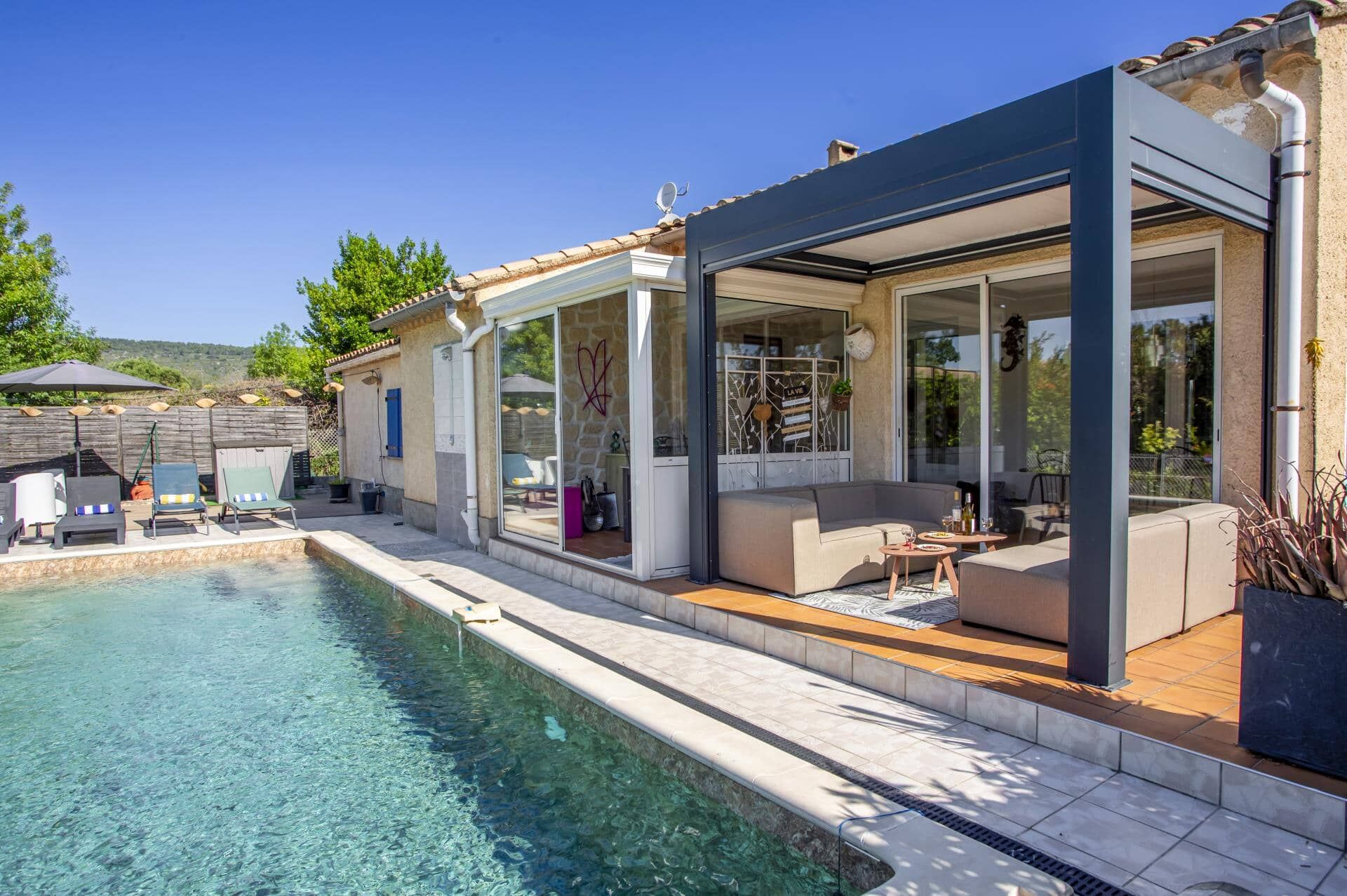 A modern house with a swimming pool, outdoor seating, and a glass-enclosed patio.