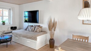 Une chambre à coucher avec un lit, une table de chevet, une télévision et un vase contenant des plantes séchées.