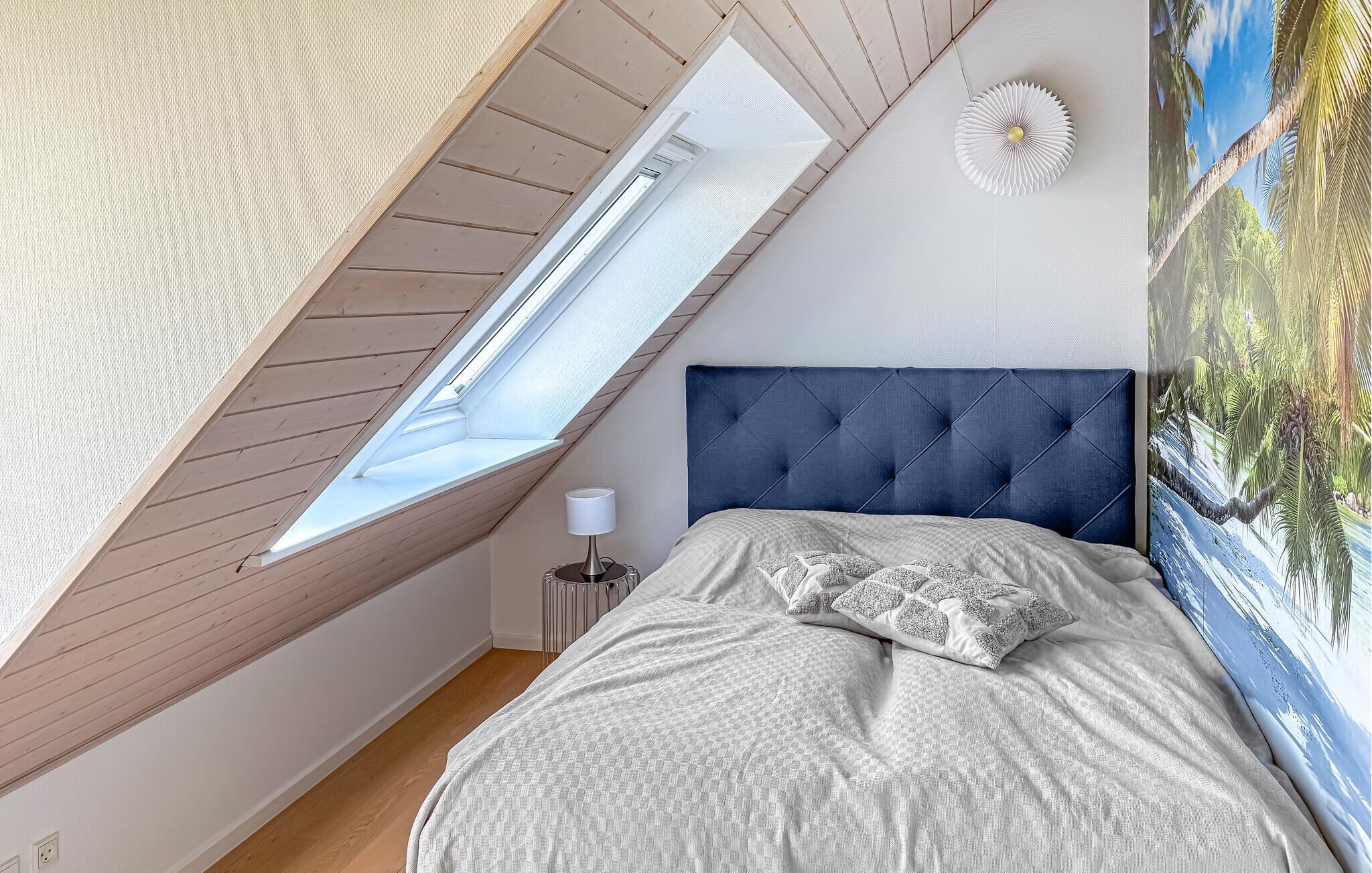 Un dormitorio con techo inclinado, una cama con cabecera capitonada, una mesita de noche, una lámpara y un aplique de pared.