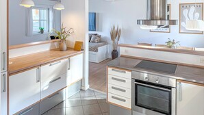 Une cuisine moderne dotée d’un four encastré, un coin repas avec une table en bois et une chambre à coucher avec un lit et une fenêtre.