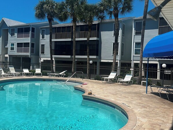 A swimming pool with lounge chairs, a blue umbrella, and a multi-story building with balconies. - Sandy Pointe #114 ~ Beach, heated pool, Preserve (Holmes Beach)