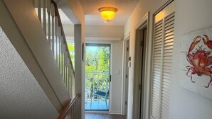Un corridoio con una scala in legno, una luce a soffitto e una porta che dà su un balcone con vista sul verde.
