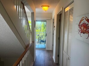 Ein Flur mit einer Holztreppe, einer Deckenleuchte und einer Tür, die auf einen Balkon mit Blick ins Grüne führt.