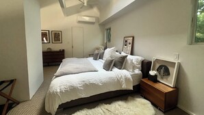 Een slaapkamer met een bed, een houten nachtkastje, een pluizig tapijt, een plafondventilator en een dakraam.