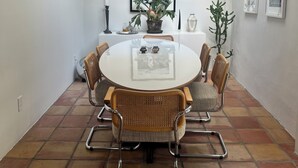 Een eetgedeelte met een ronde tafel, rieten stoelen, een potplant en ingelijste foto's aan de muur.