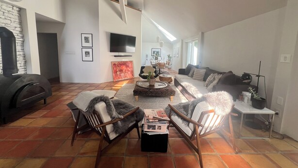 Een ruime woonkamer met een open haard, een zithoek, een salontafel en een aan de muur bevestigde televisie.