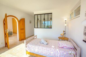 A bedroom with a bed, a bedside table, a lamp, a mirror, and a door leading to another room. - Villa Azur by Villa Plus (Sainte-Maxime)