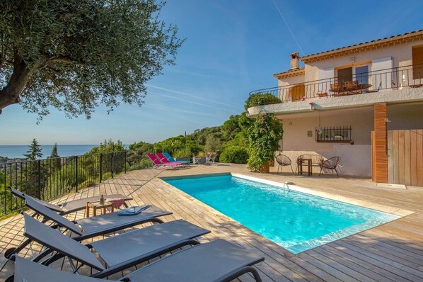 A poolside area with lounge chairs, a table, and a view of the sea. - Villa Azur by Villa Plus (Sainte-Maxime)