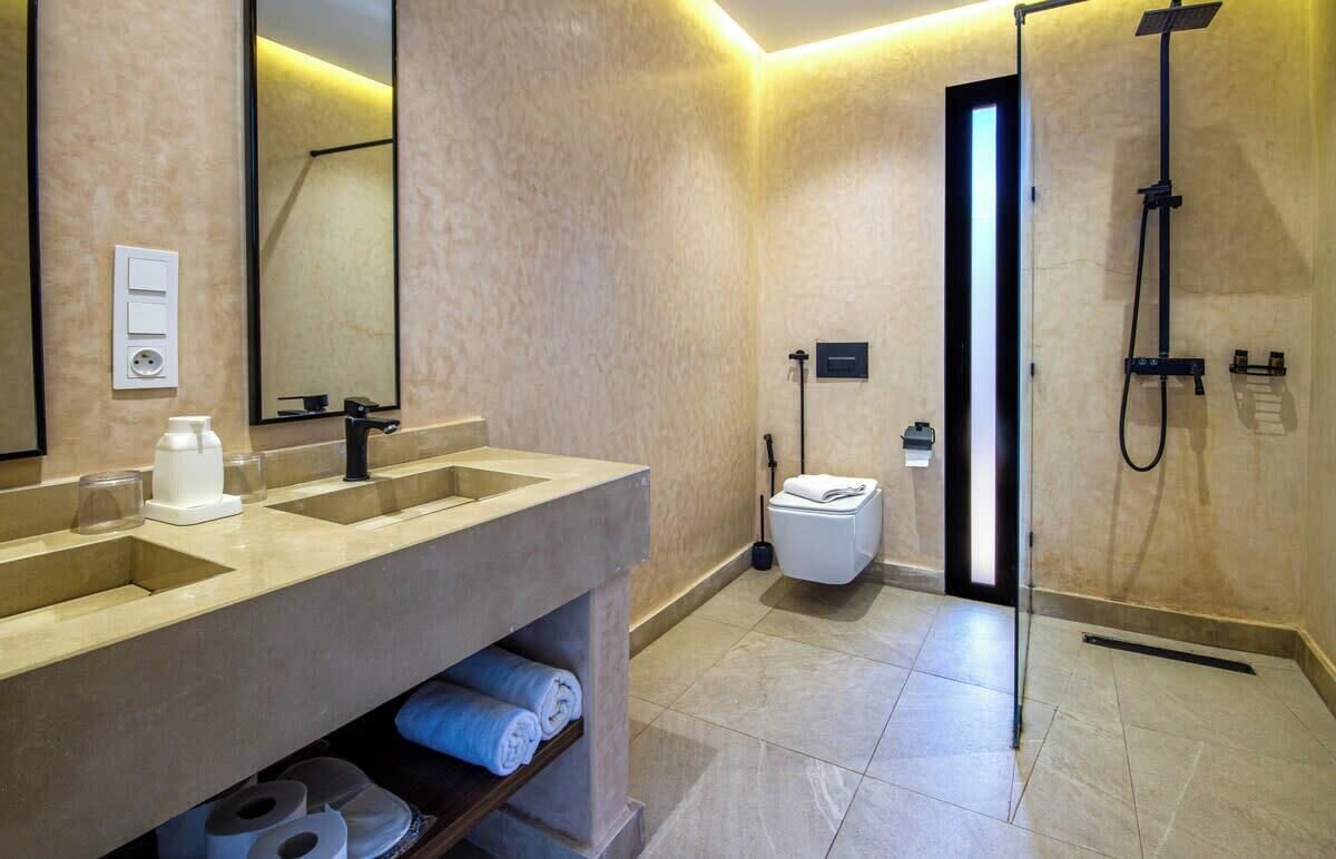 Une salle de bain moderne dotée d’un grand miroir, de deux lavabos, de toilettes et d’une douche à l’italienne.