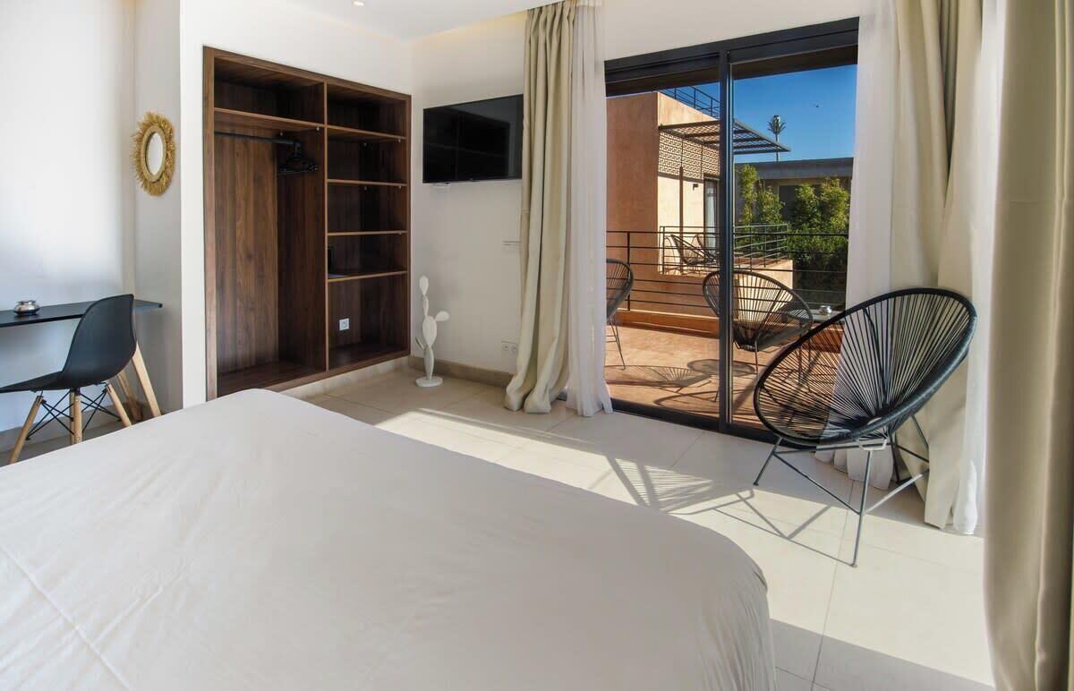 A bedroom with a bed, a desk, a chair, a wardrobe, and a balcony with chairs.