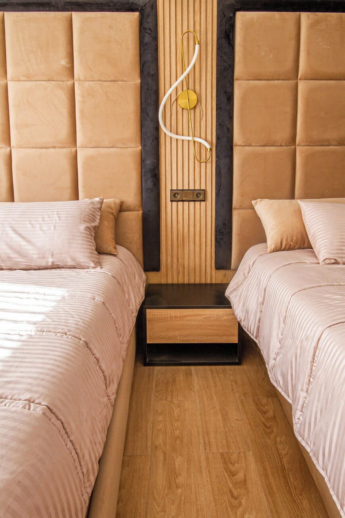 A bedroom with two beds, a wooden headboard, a bedside table, and a wall-mounted device.