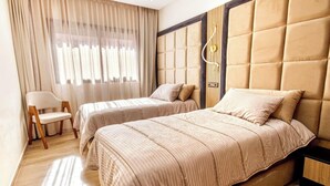 Habitación de hotel con dos camas, una silla, un escritorio y un ventanal con cortinas.