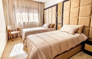 A hotel room with two beds, a chair, a desk, and a large window with curtains. - Le Nour - Beautiful 2 bedroom apt with Ac in (Marrakesh)