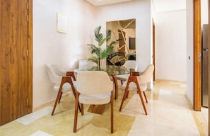 A dining area with a glass table, four chairs, a potted plant, and a wooden door. - Le Nour - Beautiful 2 bedroom apt with Ac in (Marrakesh)