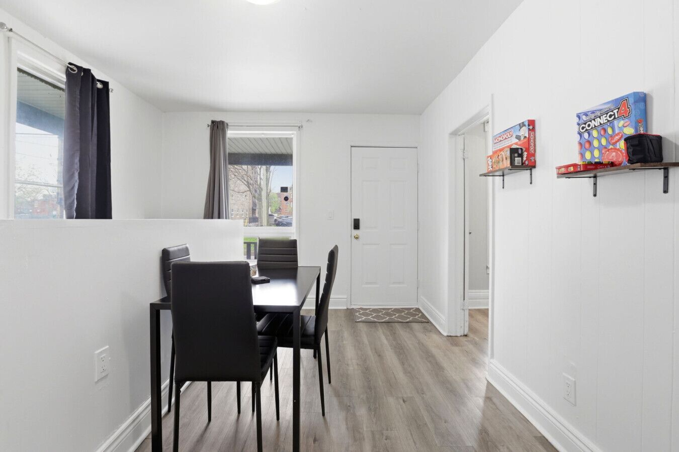 A dining area with a table and chairs, a door, and shelves with board games.