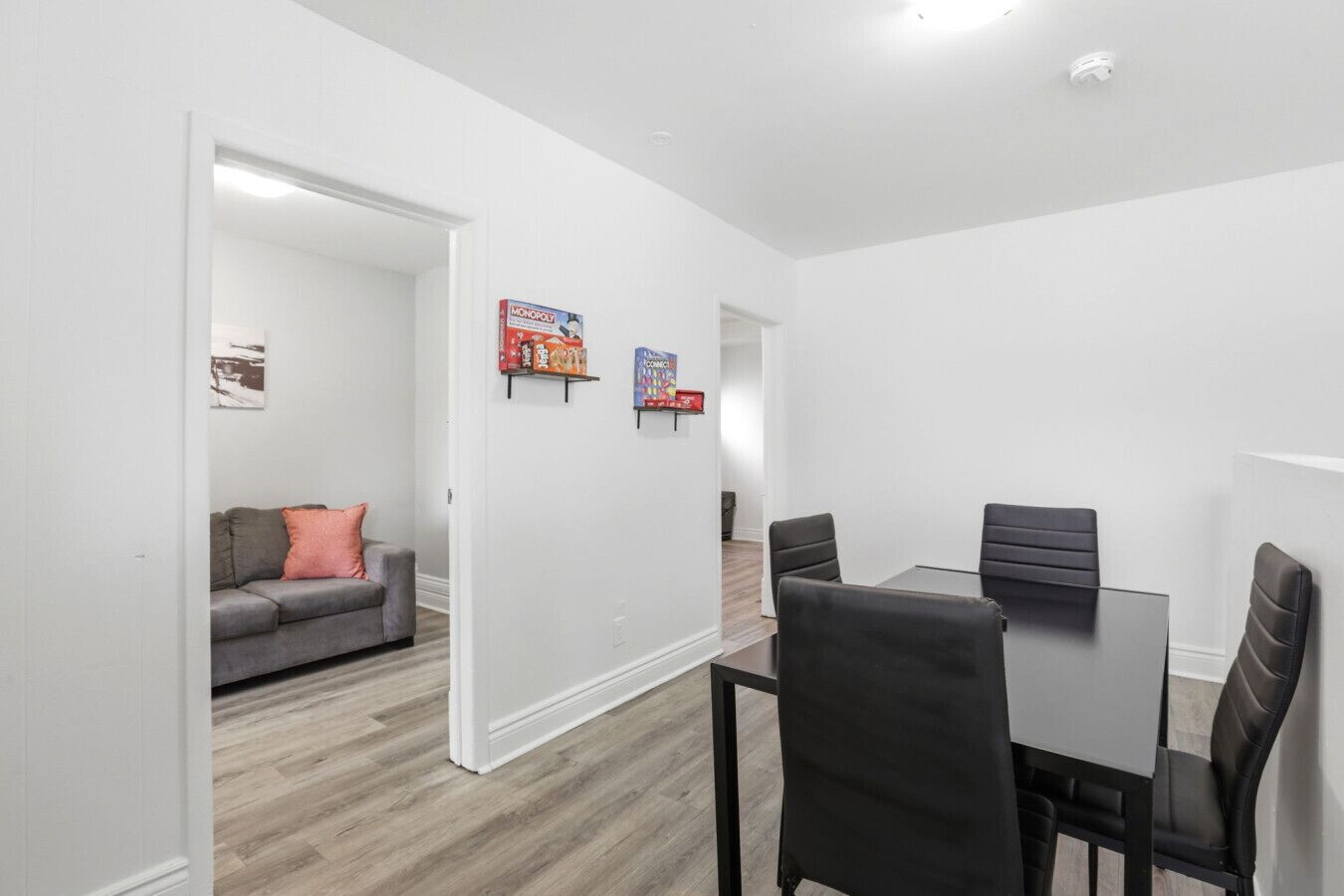 Un salon moderne avec un canapé gris, une table à manger entourée de quatre chaises et un couloir menant à une autre pièce.