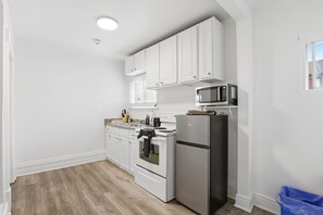 Una cocina compacta con armarios blancos, un microondas, una estufa y un refrigerador.
