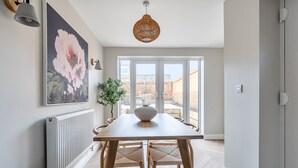 Uma sala de jantar com mesa, cadeiras, um vaso e uma pintura grande de flores na parede.