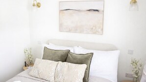 Cama bem arrumada com travesseiros brancos e verdes, cabeceira branca e pintura abstrata pendurada na parede.