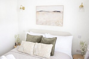 A neatly made bed with white and green pillows, a white headboard, and a wall-mounted abstract painting. - Beautifully renovated cottage in a fantastic location with free parking (Stratford-upon-Avon)