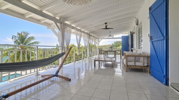 Varanda coberta com uma rede, mesa, cadeiras e vista para a piscina.