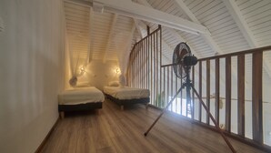 Quarto com duas camas, um ventilador e piso de madeira.