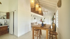 Uma cozinha espaçosa com mesa de madeira e banquetas, uma área de refeições com sofá e um teto com vigas aparentes.