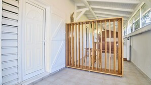 A covered outdoor area with a wooden partition, a white door, and a tiled floor. - Outbuilding in villa with sea view near Grand Bourg (Grand-Bourg)