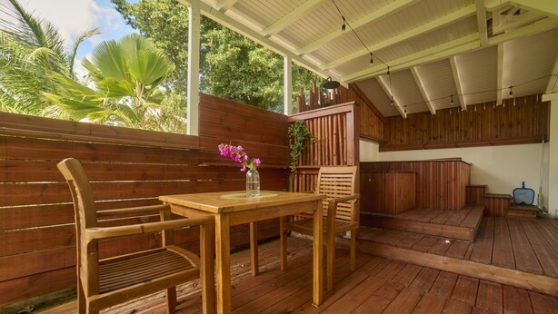 A wooden deck with a table and chairs, a wooden fence, and a view of trees. - Outbuilding in villa with sea view near Grand Bourg (Grand-Bourg)