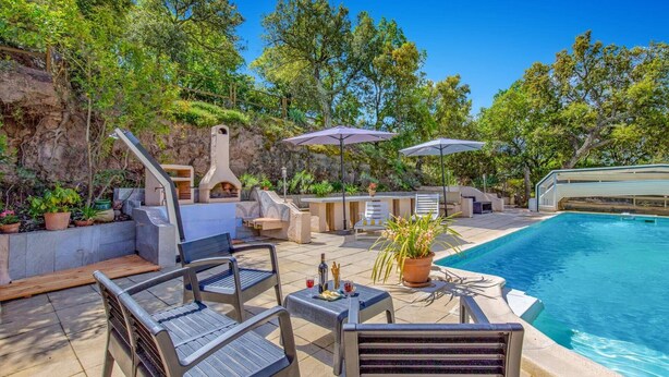 An outdoor pool area with seating, umbrellas, and a stone fireplace. - Villa Sur la Colline by Villa Plus (Les Adrets-de-l'Estérel)