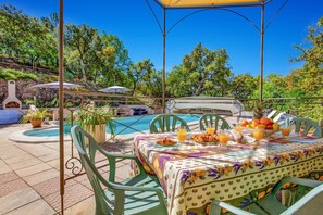 Ein Essbereich im Freien mit Pool, grünen Stühlen und Tisch, gedeckt mit Speisen und Getränken.