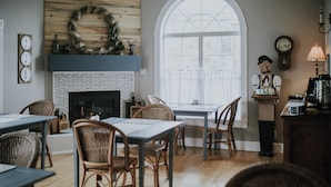 A cozy dining area with wicker chairs, a fireplace, and a large window.