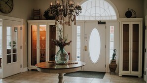 A room with a round table, a chandelier, a clock, and a large arched window.