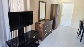Ein Zimmer mit Fernseher, Holzkommode, Spiegel und Tür.