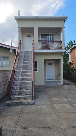 Ein zweistöckiges Gebäude mit einer Treppe zum Eingang, einem Balkon im oberen Stockwerk und einer Tür mit einem Fenster.