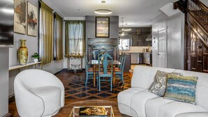 Una sala de estar moderna con comedor, una cocina al fondo y una escalera que sube a otro nivel.