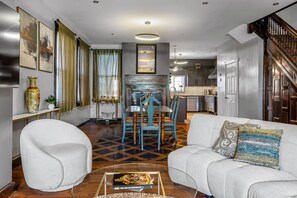 A modern living room with a dining area, a kitchen in the background, and a staircase leading to another level. - Restored Sharpsburg Gem | 2 Kings | Gourmet Kitchen | 3.5 Baths + Game Room (Pittsburgh)