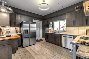 A modern kitchen with dark cabinets, stainless steel appliances, and a wooden countertop. - Restored Sharpsburg Gem | 2 Kings | Gourmet Kitchen | 3.5 Baths + Game Room (Pittsburgh)