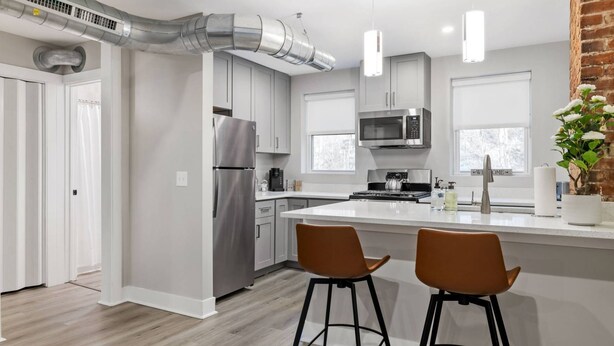 Una cocina moderna con electrodomésticos de acero inoxidable, una isla central con taburetes y una pared decorada con ladrillos.