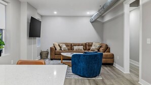 Una sala moderna con un sofá de cuero marrón, un reposapiés azul y una mesa de centro blanca.