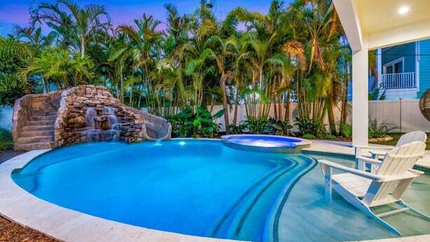 Ein Swimmingpool mit Wasserfall, umgeben von Palmen und einem Haus.