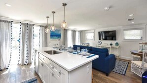 Een moderne keuken met een centraal eiland, een eethoek met een blauwe bank, en een woonkamer met een televisie.
