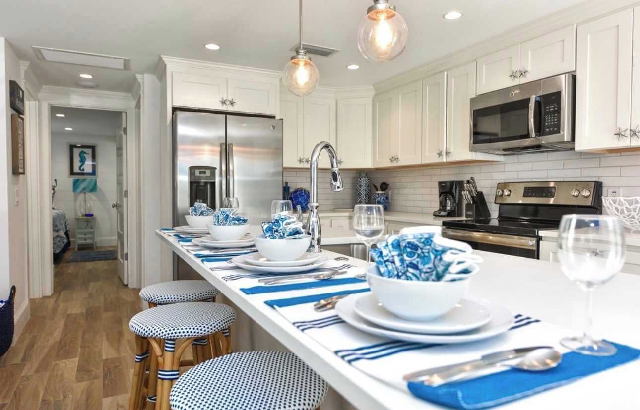A modern kitchen with white cabinets, stainless steel appliances, and a long island with blue and white decor.