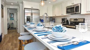 Een moderne keuken met witte kasten, roestvrijstalen apparatuur en een lang eiland, ingericht in blauw en wit.