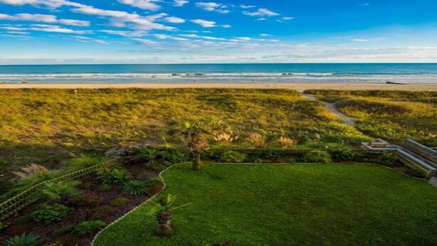 Eine Küstenlandschaft mit Strand, Grünflächen und blauem Himmel.