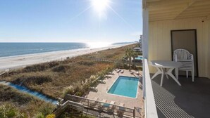 Ein Balkon mit Pool, Strandblick und Sitzgelegenheit im Freien.